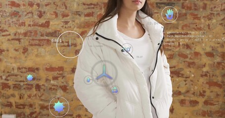 Standing woman wearing white puffer jacket by red brick wall with hologram icons and code overlays