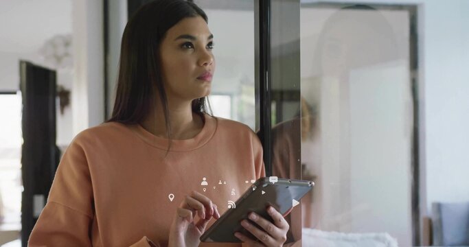 Standing adult Asian woman holding tablet by sliding door in modern living room, with white couch