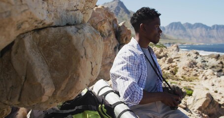 Resting hiker sitting on rocky coastal cliffs, with backpack, camera and sleeping pad, copy space