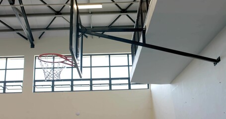 Displaying basketball hoop assembly on steel arm inside gymnasium, with exposed trusses and windows