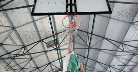 Leaping basketball player wearing green uniform dunking orange ball at gym, with rim net backboard © vectorfusionart