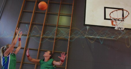 Leaping teammates in green jerseys stretching upward in school gym, with orange basketball and hoop