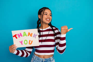 Naklejka na ściany i meble Young woman with braids holds colorful thank you sign smiles against blue background promoting gratitude joy and casual fashion Naklejka na ściany i meble Young woman with braids holds colorful thank you sign smiles against blue background promoting gratitude joy and casual fashion