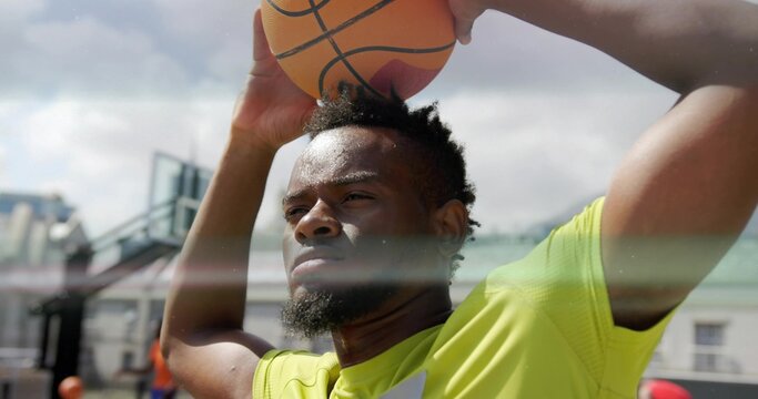 Male athlete in yellow shirt holding basketball overhead on basketball court, with hoop, backboard