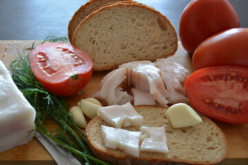 A traditional rustic snack featuring sliced pork fat, fresh bread, garlic, and tomatoes. Appetizing still life on a wooden board