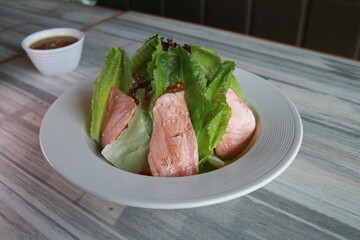 Fresh salad with salmon, a healthy and vibrant meal ready to enjoy! The plate is set on a patterned surface, with a small bowl of dressing nearby.
