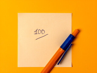 Perfect score of 100 handwritten on a yellow sticky note with a pen