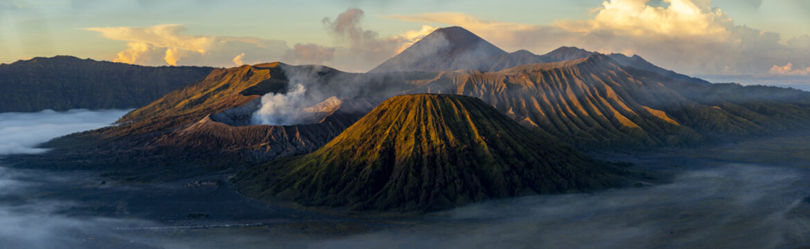 View of majestic volcanoes rising above a sea of mist, the crater emitting a plume of smoke under the golden light, Bromo, East Java, Indonesia.