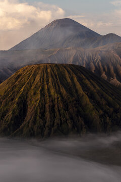View of majestic volcanic peaks rise above a sea of ethereal mist, casting long shadows across the rugged terrain in Bromo, East Java, Indonesia.
