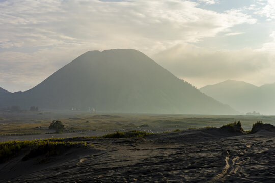 View of a majestic mountain rises from a vast, sandy plain under a soft, hazy sky, creating a serene landscape, Bromo, East Java, Indonesia.