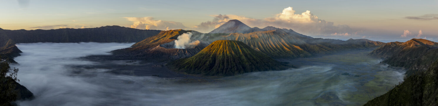 View of golden sunlight kisses the rugged peaks as wisps of fog dance through the valleys surrounding the smoking volcano, Bromo, East Java, Indonesia.