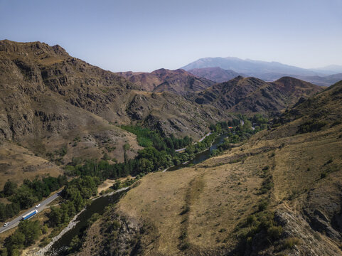 Aerial view of a winding river snaking through rugged, sun-baked mountains, where a lone highway traces its path alongside, Samtskhe-Javakheti, Samtskhe-Javakheti, Georgia.