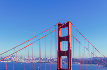Golden Gate Bridge with San Francisco Skyline in the Distance – Iconic Red Steel Structure Framing the City’s Modern Architecture Under a Clear Blue Sky, Captured in Vibrant California Travel Photo