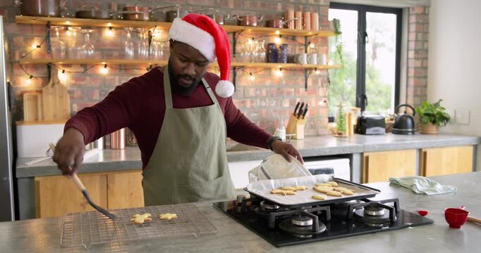After baking cookies, man wearing apron sliding cookies off griddle testing cookie taste in kitchen