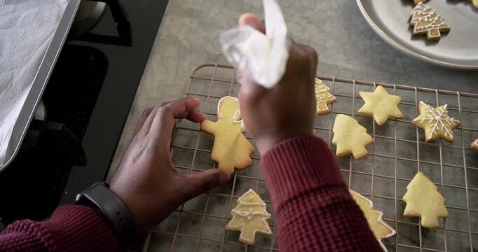 African American man placing gingerbread cookie piping icing with bag decorating shapes in kitchen