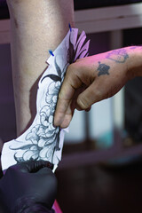 Tattoo artist preparing client's leg for floral body art, applying custom stencil design on skin
