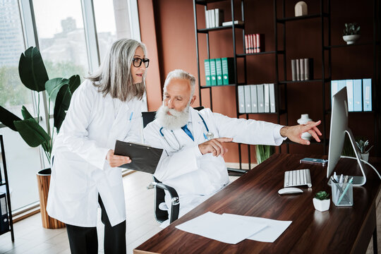 Funny medical office teamwork doctor and patient guiding elder man at a modern clinic computer desk