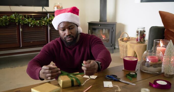 Seeing gold boxes, African American man looping ribbon, tying bow, labeling holiday gift at home