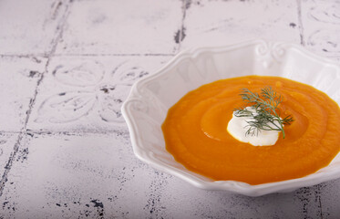 Pumpkin cream soup in a white ceramic bowl with sour cream and dill, copy space