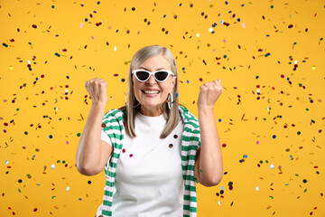Excited senior woman on yellow background with flying confetti