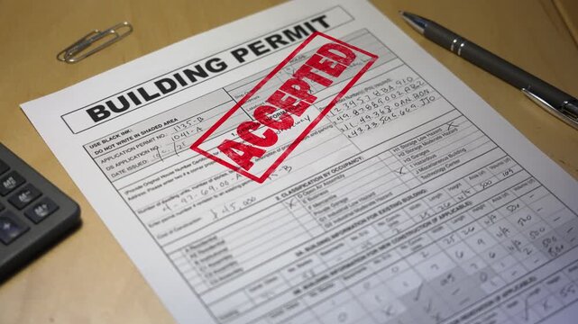 Close-up of an approved building permit stamped in red ink on a desk with a pen and calculator, symbolizing project approval and construction success. Fictional data. 14917  	