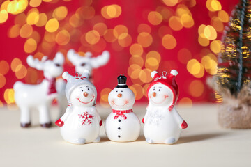 Cute decorative snowmen on white table against red background with blurred lights, closeup