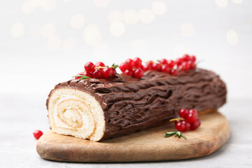 Delicious Yule log (traditional Christmas cake) with redcurrant on table against blurred lights, closeup. Bokeh effect