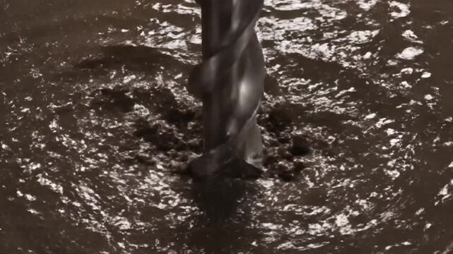Drilling into thick dark liquid with splashes and ripples.