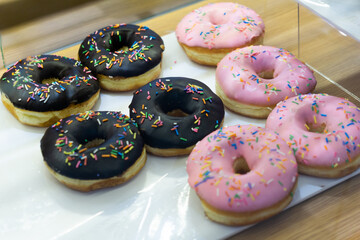 A display of donuts with pink and chocolate frosting, topped with colorful sprinkles, arranged on a white tray