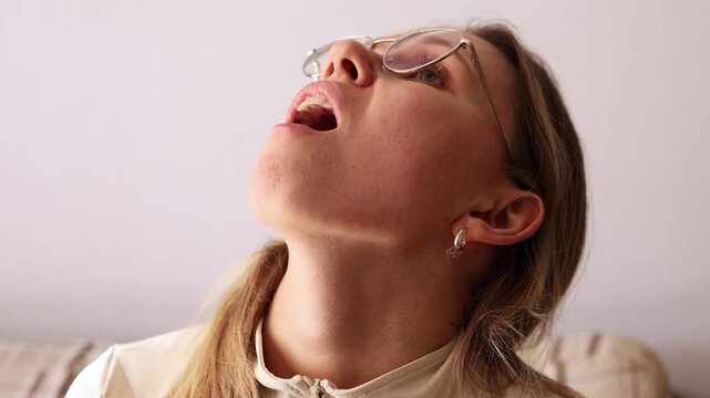 Girl in glasses tilting head back and gargling, close-up.