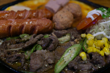 A appetizing plate of assorted foods, including grilled sausage, meat slices, vegetables, corn, fresh tomato, shredded cabbage with mayonnaise, and fried items.