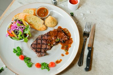 A beautifully plated steak dinner ready to eat. Steak, bread, salad and sauce