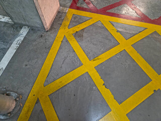 Overhead view of a concrete floor with a large yellow cross-hatch marking and worn red and white lines nearby.