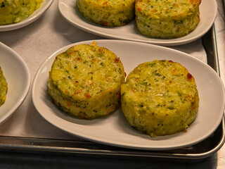 Close-up of two round, baked vegetable medallions served on a small white platter in a food service setting.
