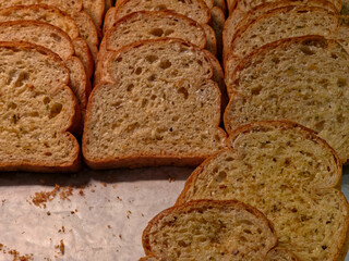 Close-up, high-angle view of multiple overlapping slices of toasted or buttered garlic bread, seasoned with visible herbs, arranged on a piece of parchment paper.

