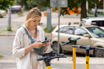 woman using smartphone while standing near electric scooter on city street