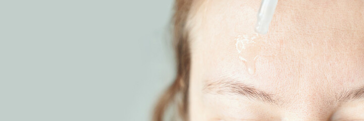 Naklejka premium Female applying skincare serum to forehead with dropper on clear background.