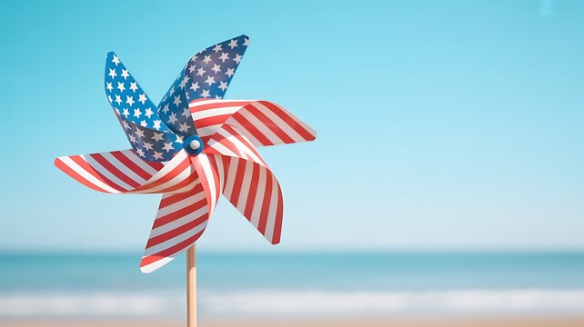 A vibrant pinwheel adorned with the american flag pattern rests on a beach, set against a serene ocean and clear blue sky