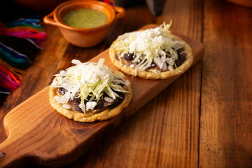 Sopes. Mexican typical food prepared with flattened fried corn dough covered with refried beans, green or red sauce, lettuce, cheese, onion and sour cream. Mexican antojitos.