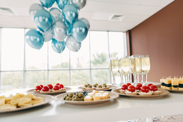 Elegant corporate gathering with appetizers and drinks against a bright office environment with blue balloons