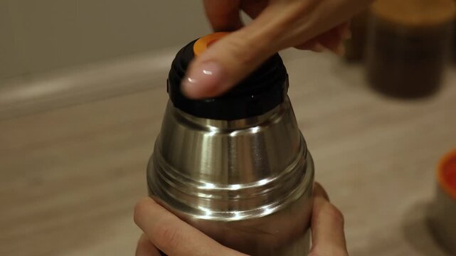 A person demonstrates how to correctly close a stainless steel thermos. The focus is on ensuring a tight seal to maintain beverage temperature while using a simple twist motion.