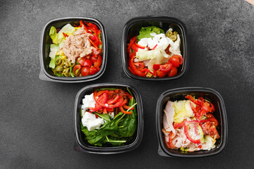 Mixed salads with fresh vegetables meat cheese and greens in black containers for restaurant delivery or meal prep concept