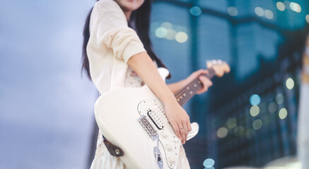 Gen z asian woman playing electric guitar busking street music at outdoor night city wearing y2k...