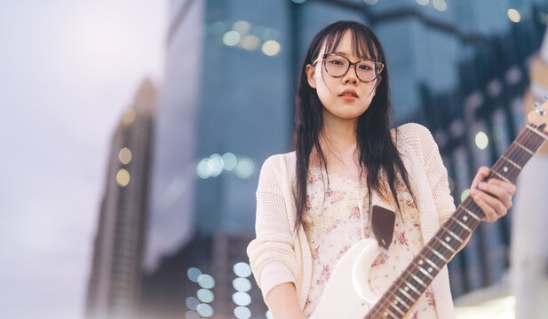 Gen z asian woman playing electric guitar busking street music at outdoor night city wearing y2k fashionable style