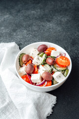 Greek salad with feta cheese olives cucumbers tomatoes and onions in white bowl on dark background with napkin