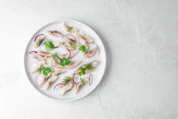 Marinated herring slices with red onion and herbs on white plate over light background