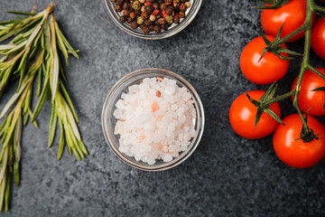 Pink himalayan salt with cherry tomatoes pepper and rosemary on dark background