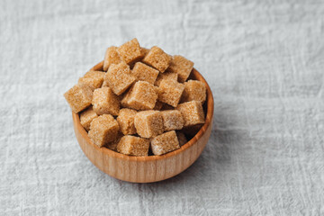 Brown sugar cubes in a wooden bowl on a textured gray surface