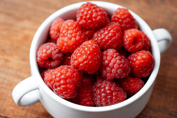 Raspberries in white bowl. on wooden table for rustic food styling or organic eating concept
