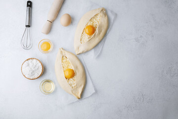 Top view of two khachapuri breads with eggs and flour on white kitchen surface
